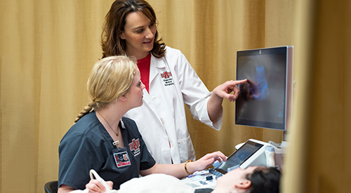 A teacher pointing something out to a student during an ultrasound